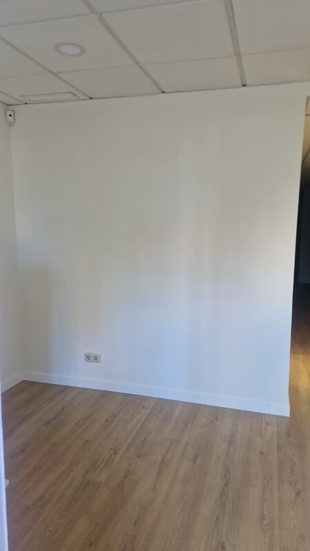 La pared de la sala de espera antes: blanca y vacía, con el suelo de madera y el techo de placas.