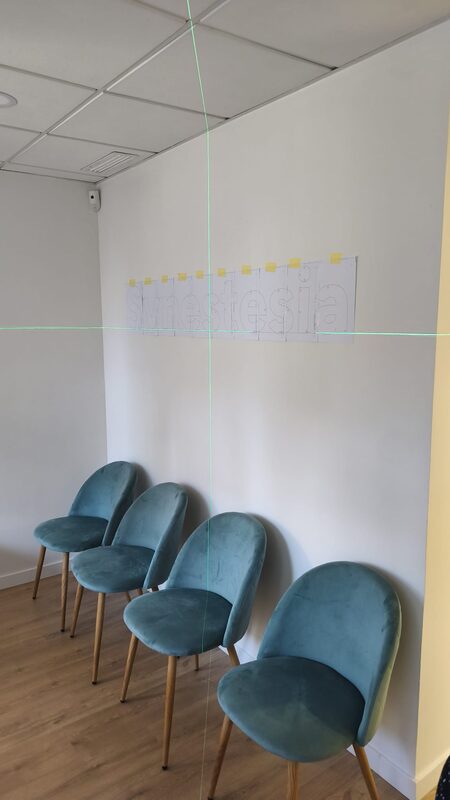 La plantilla de papel pegada a la pared sobre las sillas, nivelada con las líneas verdes de un nivel láser.